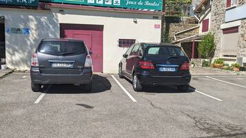 Un estacionamiento con dos autos estacionados frente a un edificio que tiene un letrero con la frase 'Chambres Climatisees' y 'Jeux de Boules'.