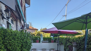 An outdoor patio area with tables and chairs, surrounded by greenery and a low wall. - AUBERGE DES PINS (Aubenas)