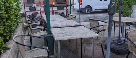 An outdoor seating area with tables and chairs, umbrellas, and a white van in the background.