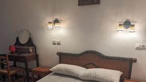 A bedroom with a large bed, two bedside tables, a desk with a chair, a wall-mounted lamp, and a painting. - AUBERGE DES PINS (Aubenas)