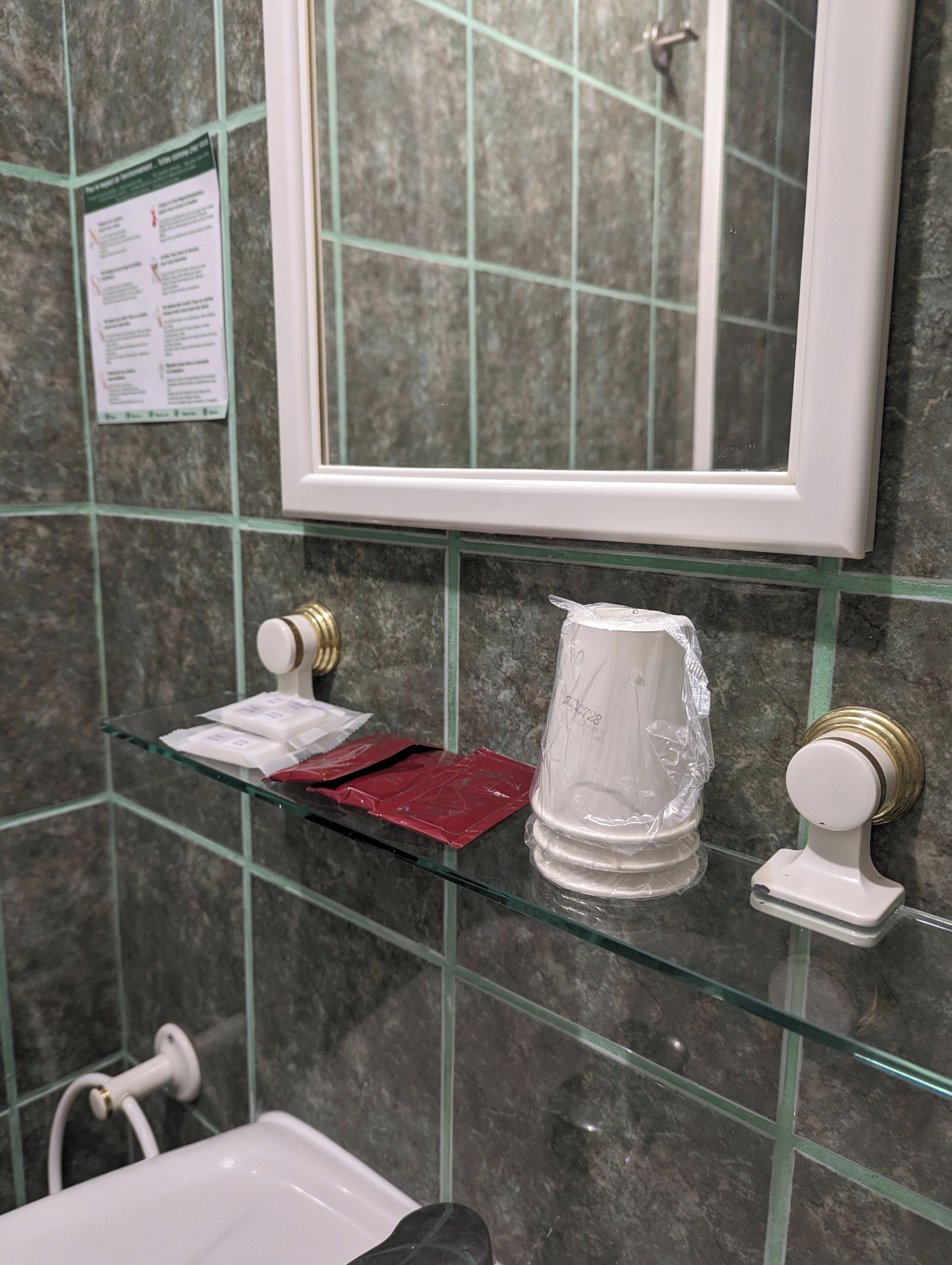 A bathroom with a glass shelf holding toiletries, a white bathtub, and a mirror above the shelf.