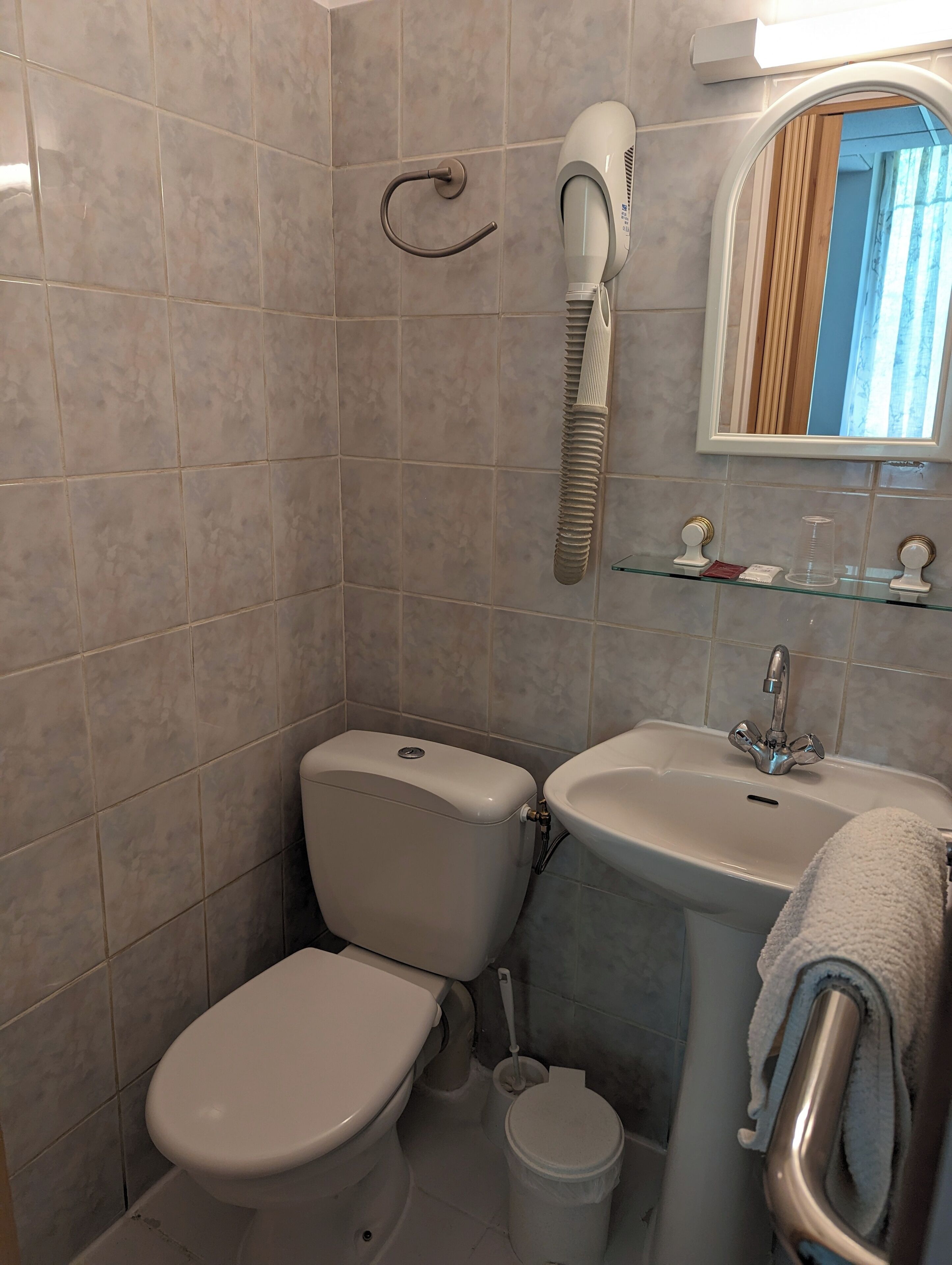 Un baño con inodoro, lavamanos y secador de pelo montado en la pared.