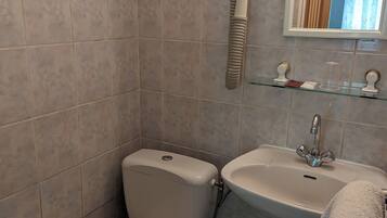 Un baño con inodoro, lavamanos y secador de pelo montado en la pared.