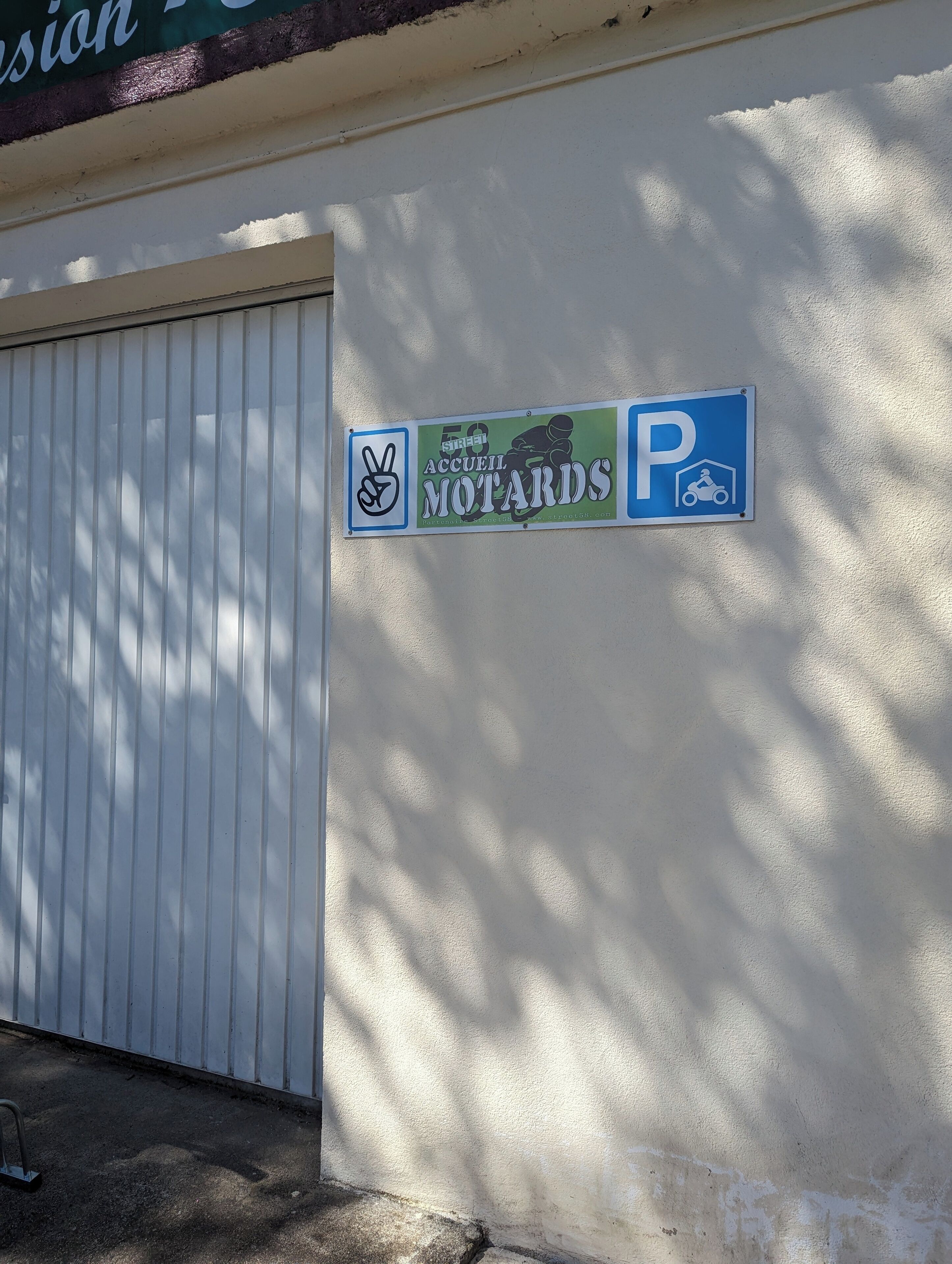 Une pancarte annonçant un événement pour motards, une porte de garage blanche et des ombres sur un mur.