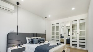 A modern bedroom with a large bed, bedside tables, a wardrobe, and a ceiling-mounted air conditioner.