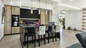 A modern kitchen with a central island, pendant lights, and a dining area with patterned chairs.