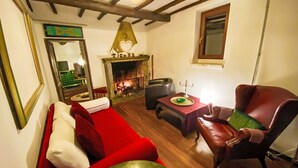 Een gezellige woonkamer met een rode bank, een groene fauteuil, een open haard en een spiegel aan de muur.