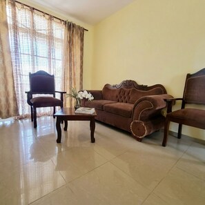 A living room with a brown sofa, a wooden coffee table, a chair, and a window with curtains. - Cozy Apartment in Gated Community Costambar, Puerto Plata (Puerto Plata)
