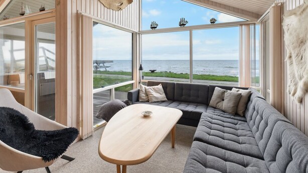 Een modern interieur met een groot raam met uitzicht op zee, een gezellige zithoek en een houten plafond.