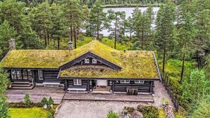 Mökki, jonka katto on vihreä, ja jonka ympärillä on metsää ja järvi.