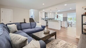 Ein modernes Wohnzimmer mit einem blauen Ecksofa, einem Couchtisch und einer Treppe, die in eine Küche und einen Essbereich führt.