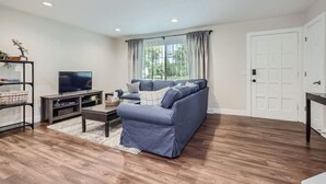 Ein Wohnzimmer mit einem blauen Sofa, einem Fernseher auf einem Schrank und einem Bücherregal.