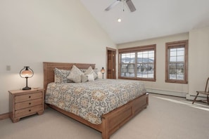 A bedroom with a wooden bed, a nightstand, a lamp, and large windows with a view of mountains. - Luxe MTN Escape 15 min to Winter Park Base (Tabernash)