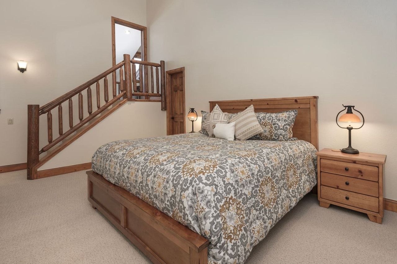 A bedroom with a wooden bed, a nightstand, a lamp, a mirror, and a staircase.