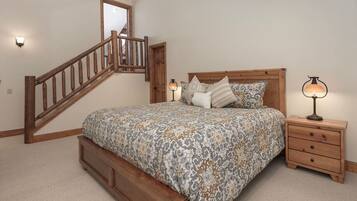 A bedroom with a wooden bed, a nightstand, a lamp, a mirror, and a staircase.