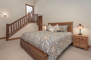 A bedroom with a wooden bed, a nightstand, a lamp, a mirror, and a staircase. - Luxe MTN Escape 15 min to Winter Park Base (Tabernash)