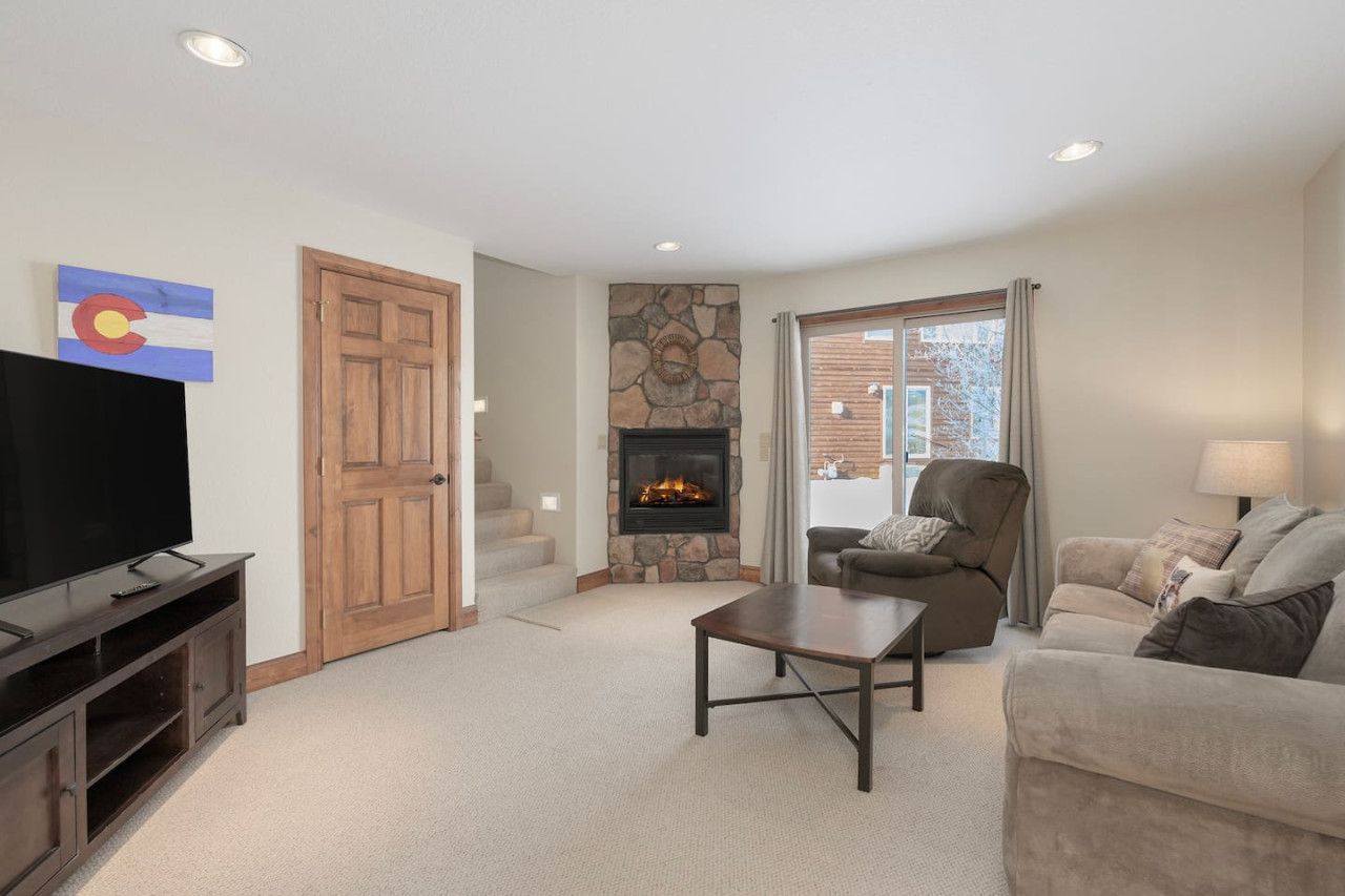 A living room with a stone fireplace, a television, a couch, and a chair.