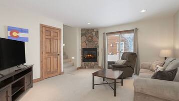 A living room with a stone fireplace, a television, a couch, and a chair.