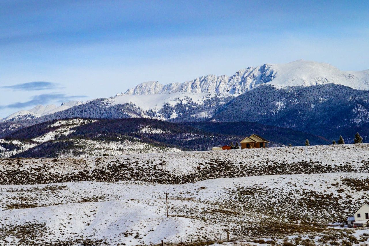 A snow-covered landscape with a mountain range in the background and a small house in the foreground.