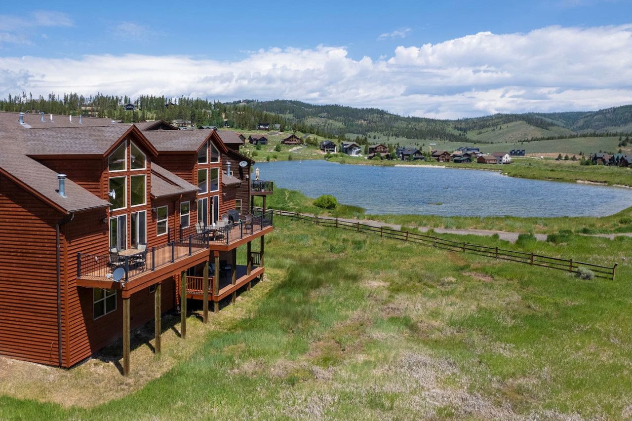 A wooden cabin with a balcony overlooking a lake and hills.