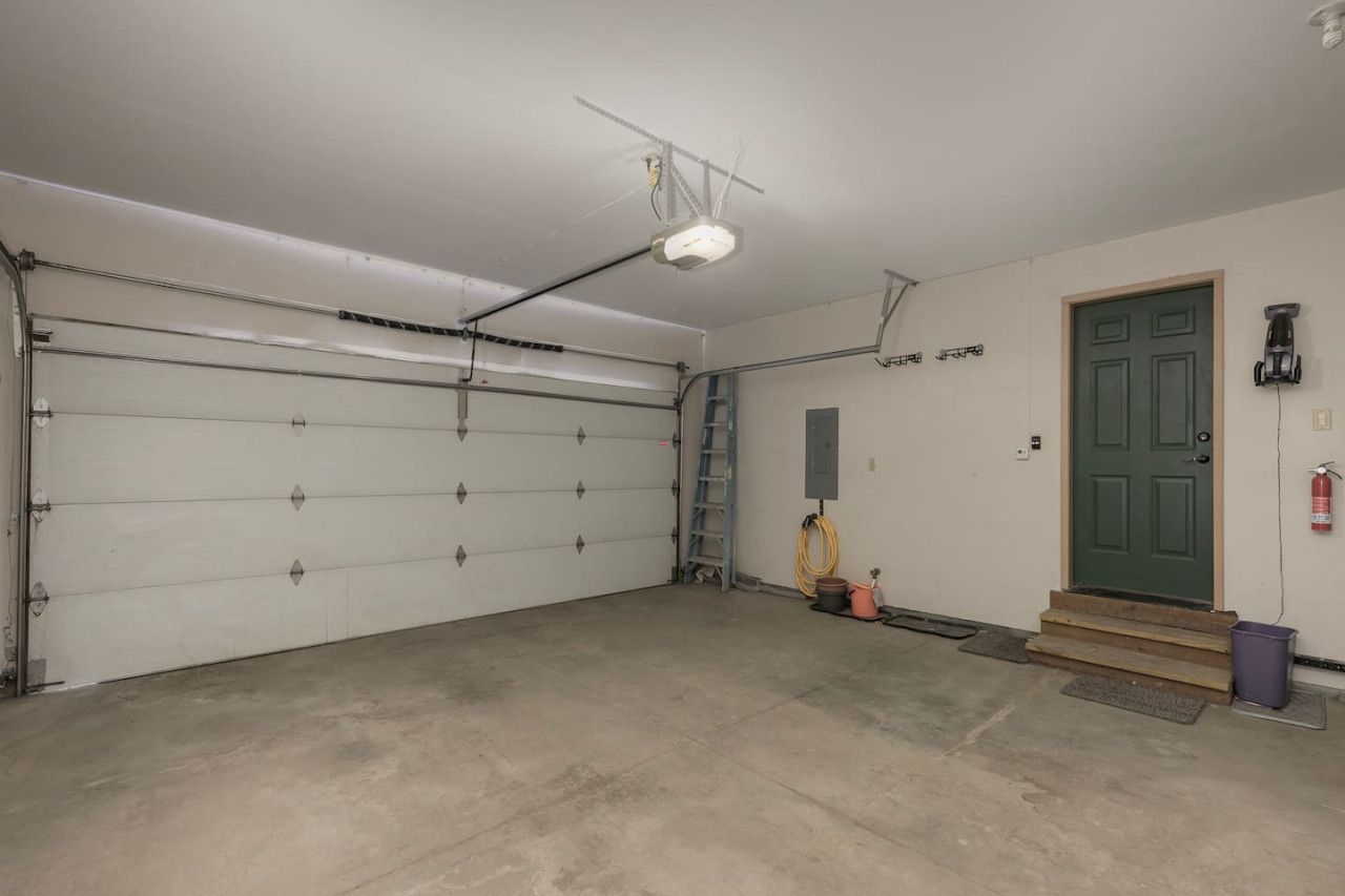 A garage with a closed white garage door, a ladder, a green door, and a fire extinguisher mounted on the wall.