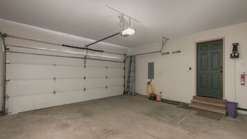 A garage with a closed white garage door, a ladder, a green door, and a fire extinguisher mounted on the wall.