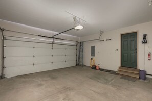 A garage with a closed white garage door, a ladder, a green door, and a fire extinguisher mounted on the wall. - Luxe MTN Escape 15 min to Winter Park Base (Tabernash)