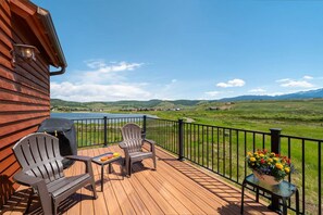 Une terrasse en bois avec deux fauteuils Adirondack, un barbecue et une table sur laquelle se trouvent un livre et des collations. Un pot de fleurs est posé sur le bord de la terrasse.