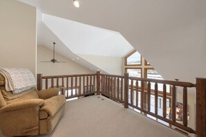 A spacious loft bedroom with a high ceiling, a wooden railing, a ceiling fan, and a large window offering a view of the outdoors. - Luxe MTN Escape 15 min to Winter Park Base (Tabernash)