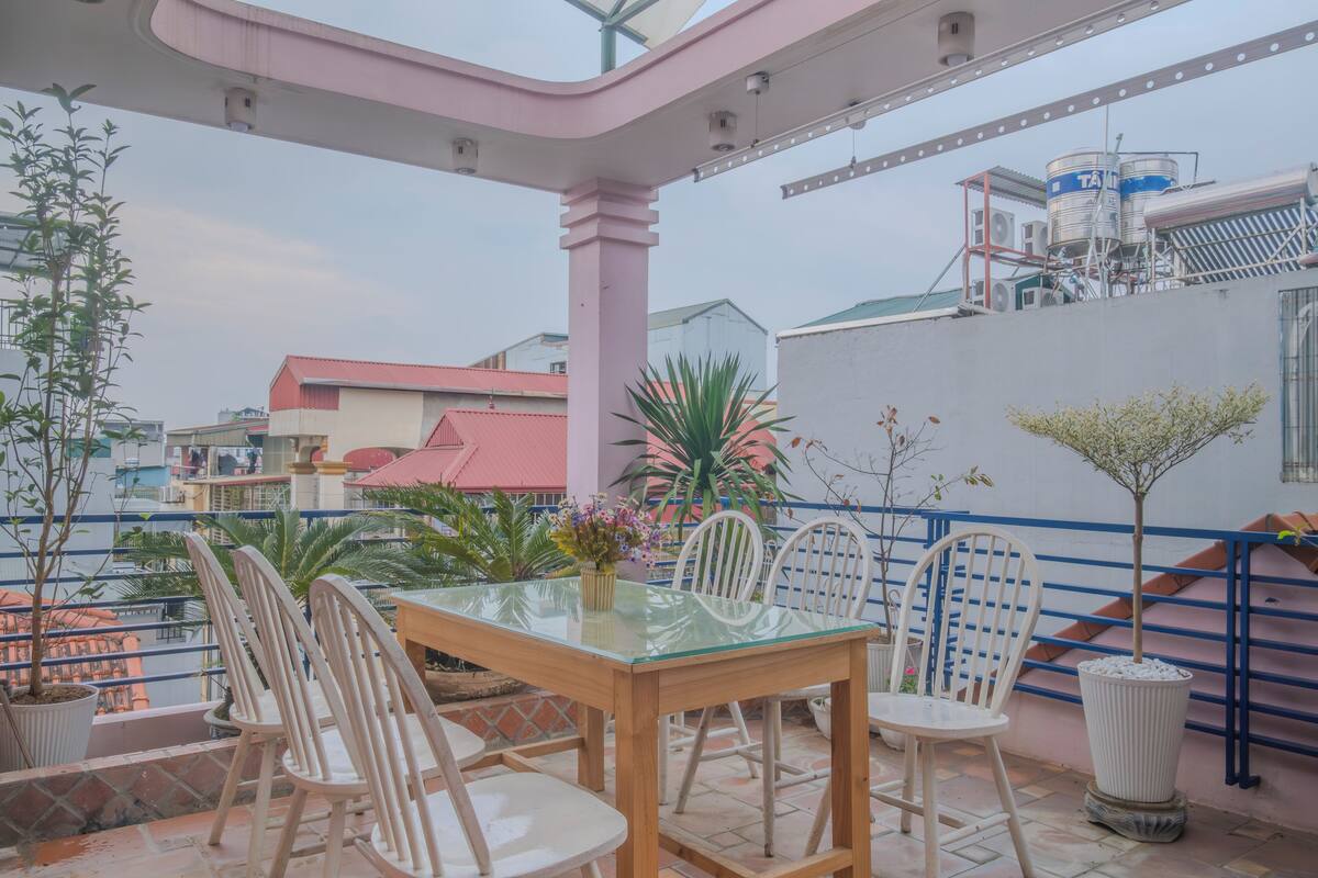 An outdoor patio with a glass-top table and white chairs, surrounded by potted plants and a staircase.