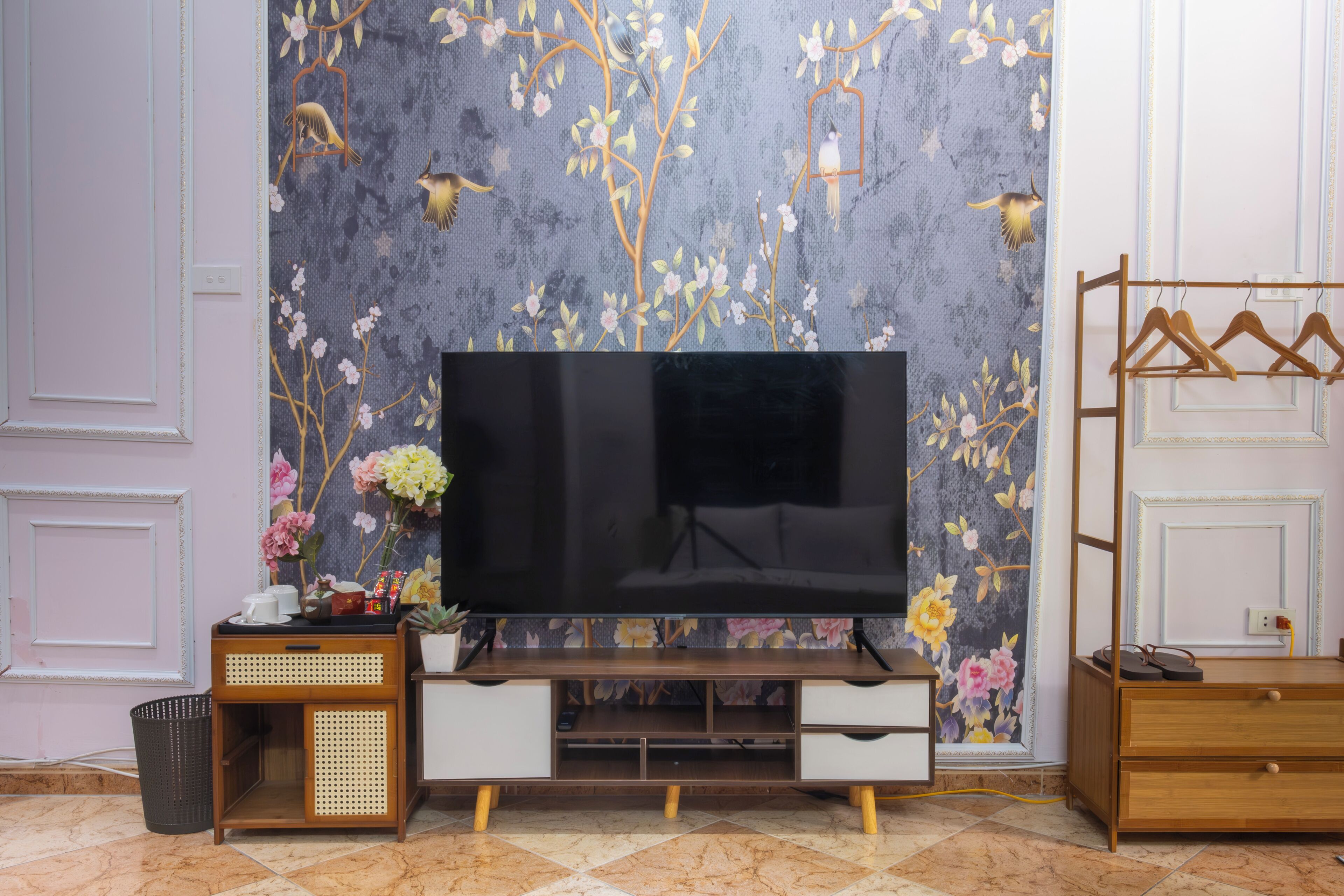 A living room with a flat-screen TV, wooden furniture, and a floral wallpaper.