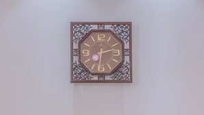 Um quarto com um relógio fixado na parede, uma mesinha com abajur e duas cadeiras com almofadas decorativas.