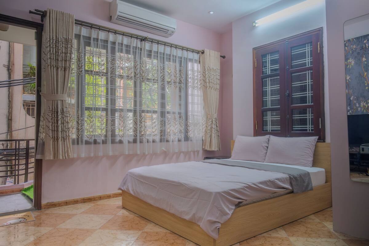 A bedroom with a bed, a window with curtains, an air conditioning unit, and a door with glass panels.