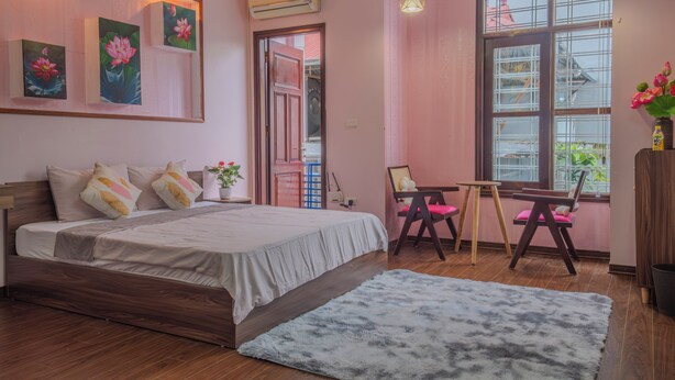 Quarto com cama, escrivaninha e cadeira. Há uma janela com vista para edifícios.