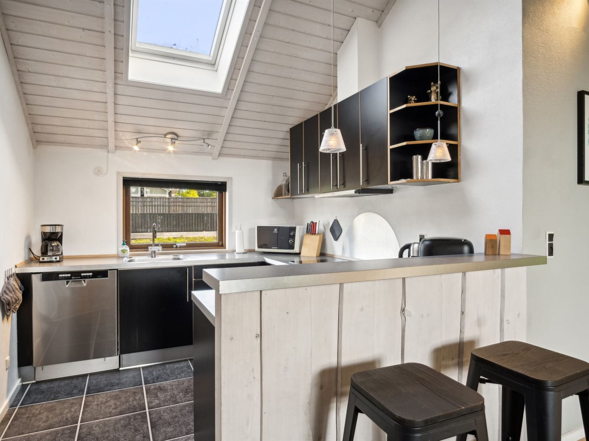 Una cocina moderna con tragaluz, lavavajillas, cafetera y una pequeña isla con taburetes.