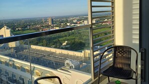 Ein Balkon mit zwei Stühlen und einem kleinen Tisch, mit Blick auf eine Stadtlandschaft aus Gebäuden und Grünflächen.