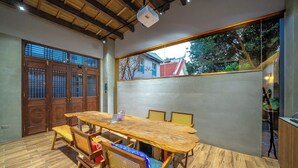 A dining area with a wooden table and chairs, a projector, and a view of the outside through a large window. - Komorebi Souseki (Tainan)