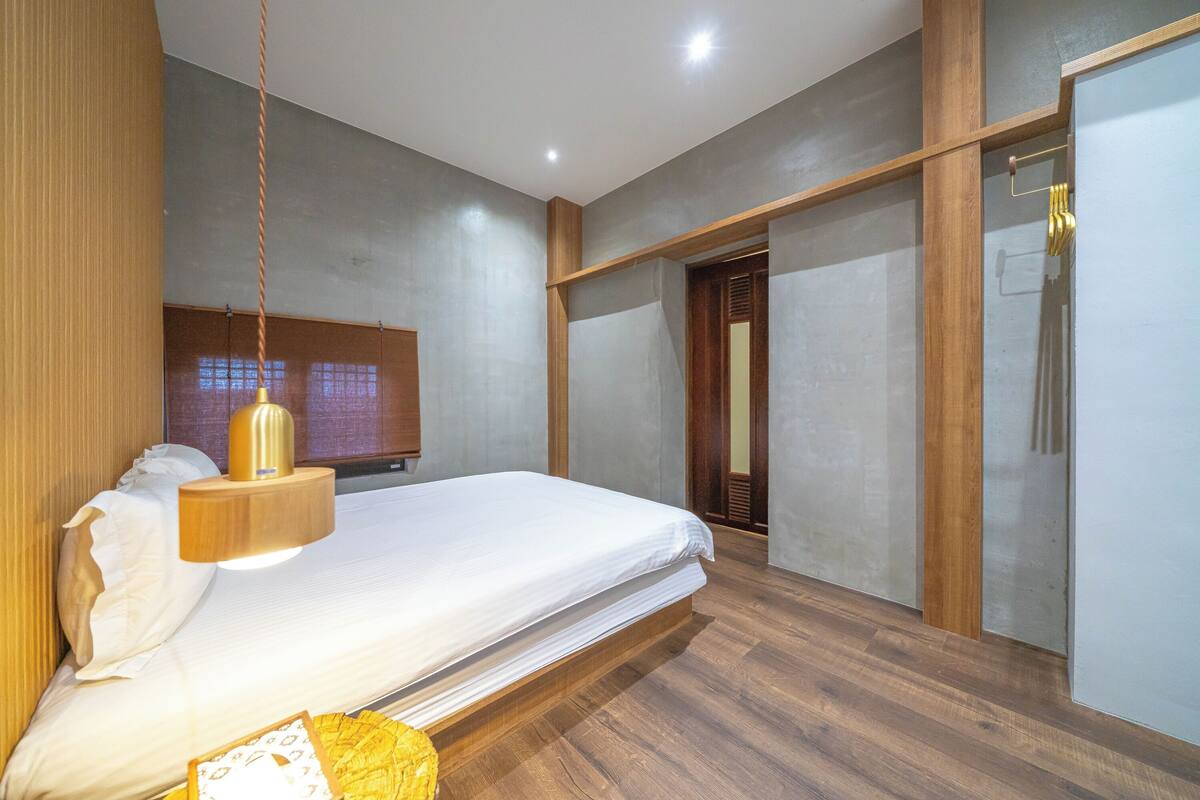 Un dormitorio moderno con cama, cabecero de madera y lámpara colgante.