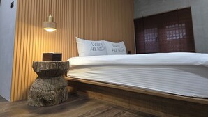 A modern bedroom with a wooden slat wall, a bed with white bedding, and a small wooden stool. - Komorebi Souseki (Tainan)