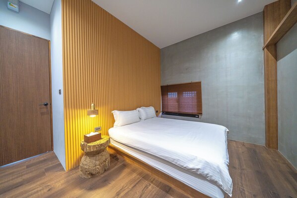 A bedroom with a wooden floor, a bed with white bedding, a wooden headboard, a bedside table with a lamp, and a window with blinds. - Komorebi Souseki (Tainan)