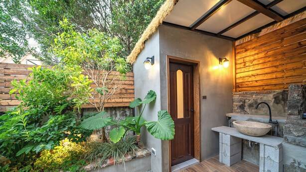 A rustic bathroom with a stone sink, wooden door, and a small garden area with plants. - Komorebi Souseki (Tainan)