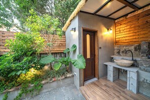 Un bany rústic amb un rentapeus de pedra, una porta de fusta i una petita zona de jardí amb plantes.