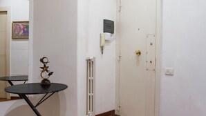Una habitación con una puerta blanca, un radiador, una pequeña mesa con un objeto decorativo y un cuadro en la pared.