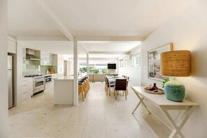 A modern kitchen with white cabinetry, a dining area with a table and chairs, and a large window providing a view of the outdoors.