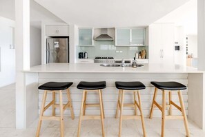 A modern kitchen with white cabinetry, a stainless steel refrigerator, a gas stove, and three black stools.