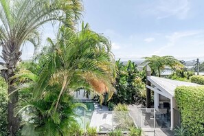 A modern house with a pool, surrounded by lush greenery and palm trees.