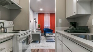 A compact kitchen with white appliances, a dining area with a red curtain, and a small seating space.