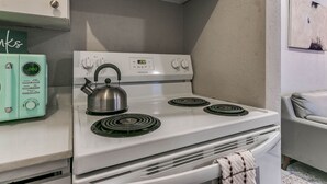 A kitchen with a white stove, a green microwave, and a kettle on the stove.