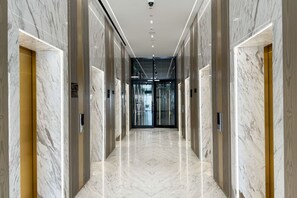 Un couloir moderne aux murs de marbre, dotĂ© dâun sol poli et dâune entrĂ©e en verre pour lâascenseur.