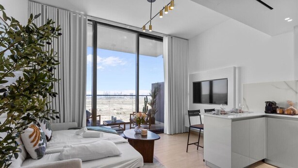 Una camera d'albergo moderna con un'ampia finestra, un letto, un piccolo angolo ristoro e una televisione.